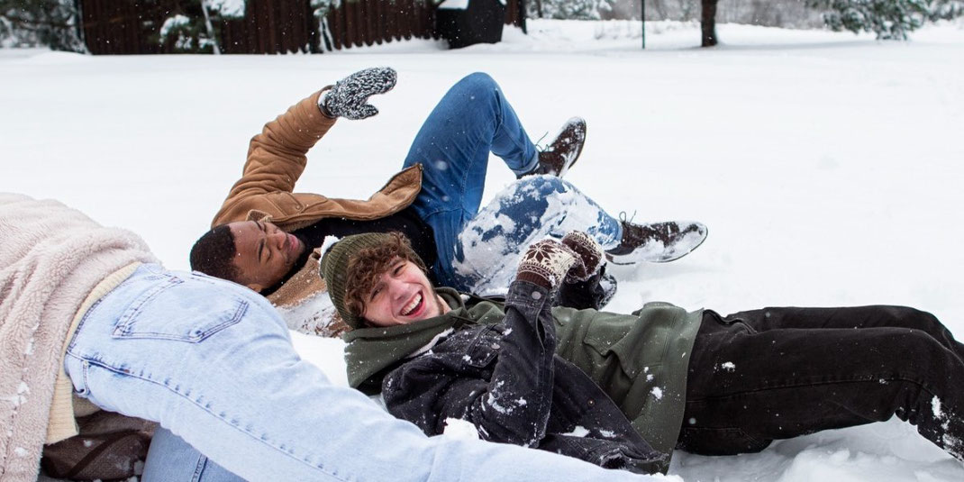 Drei junge Menschen lachen und spielen gemeinsam im tiefen Schnee eines Winterwaldes.
