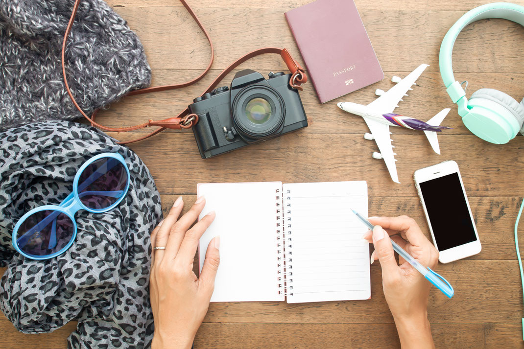 Reiseplanung mit Kamera, Pass, Modellflugzeug, Smartphone, Kopfhörer und Notizbuch – Vorbereitungen für die nächste Flugreise festhalten