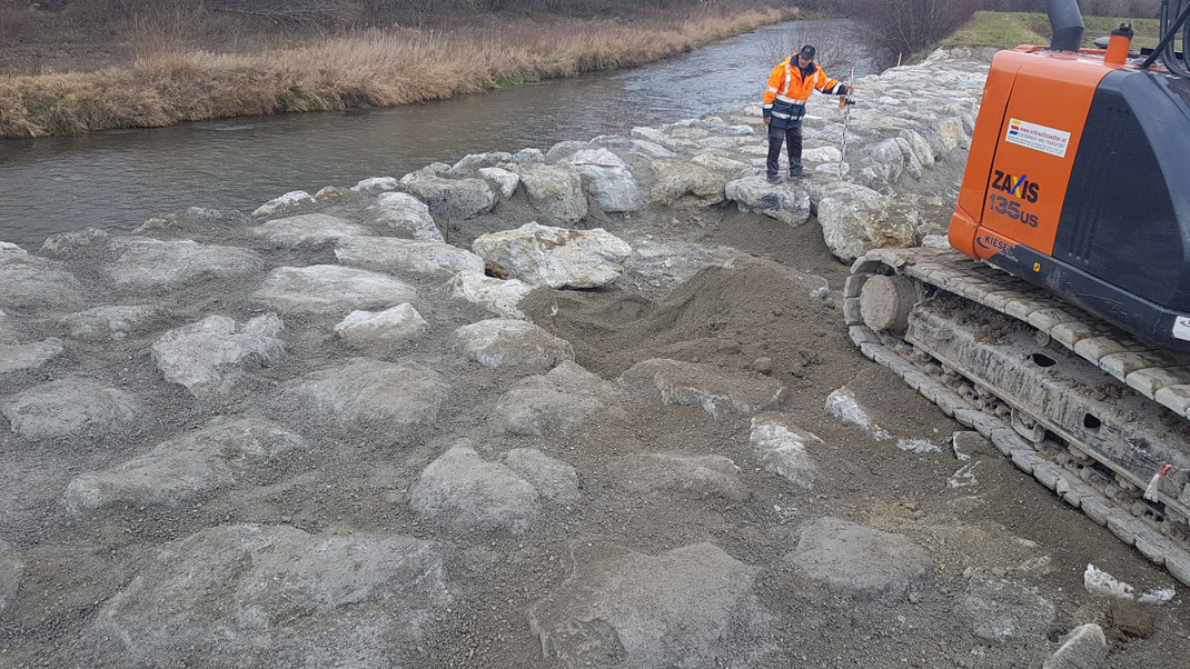 Flussufer mit Steinen befestigt mit einem Arbeiter und einem Bagger darauf.