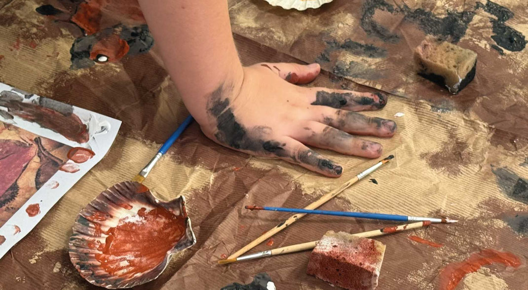 mani di bambino che esplora materiali per pitturare durante un laboratorio sulle pitture rupestri