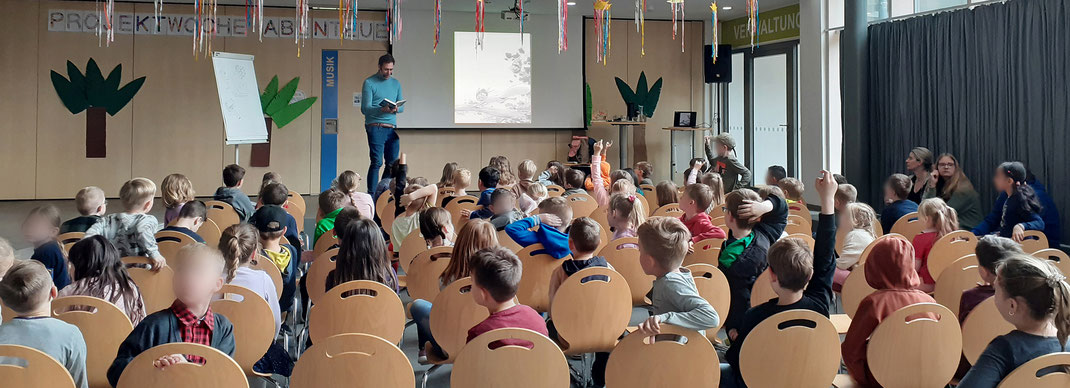 Die Schulaula der Grundschule am Wildfang. Kinderbuchautor Michael Mantel liest vor etwa 80 Kindern aus seinem Buch "Unterholz-Ninjas".