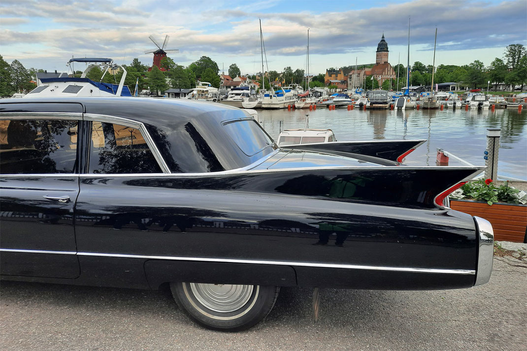 Ein schwarzer amerikanischer Oldtimer steht am Freizeithafen von Strängnäs. Im Hintergrund sind eine alte rote Mühle und der Dom von Strängnäs zu sehen.