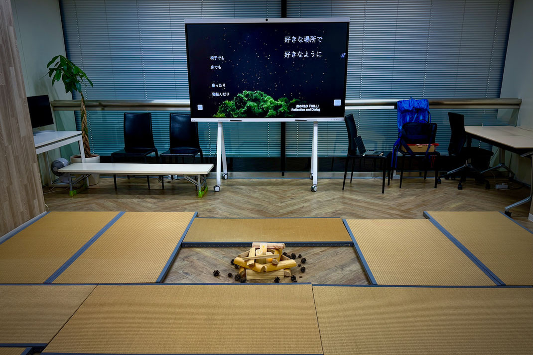畳を敷き詰めた会議室で、蝋燭の焚き火と夜の森の映像が投影された空間