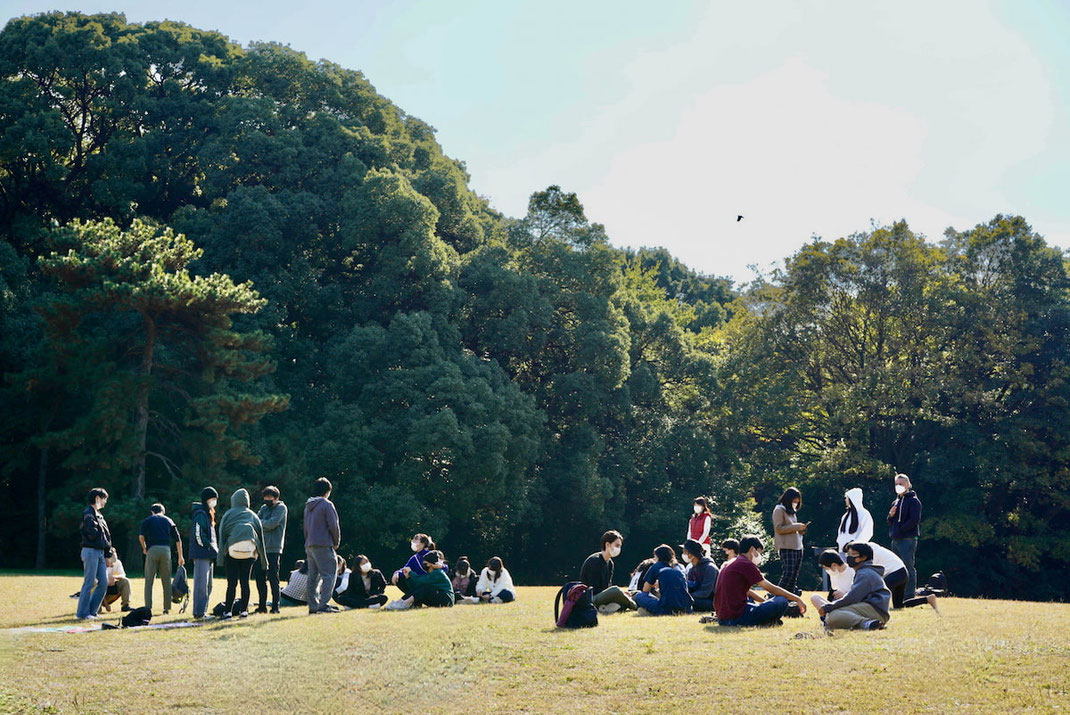 空の下に広がる芝生の上に集まって、リラックスして談笑するシーン