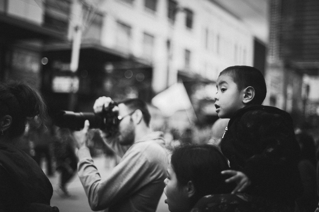 an asian boy looking excited at a Halloween parade on the shoulders of his mother