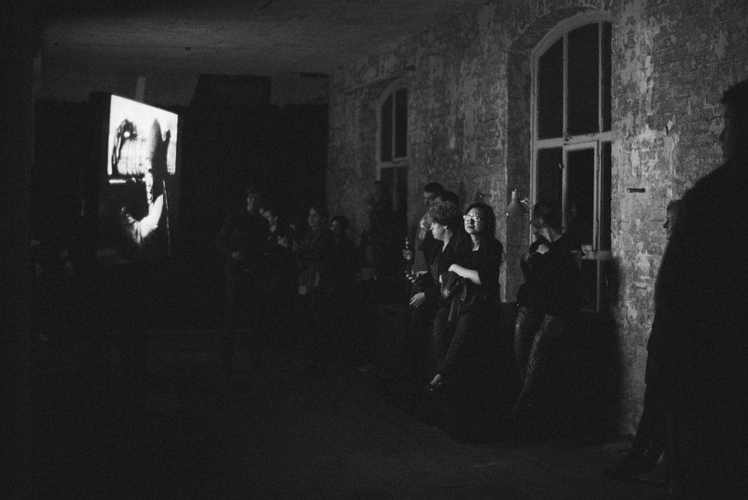a black & white image of a group of people watching the contributions to the awards on a large monitor