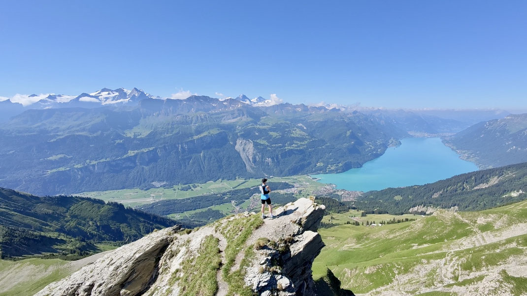 Trailrunner geniesst von einem spektakulären Felsvorsprung beim Höch Gumme die Aussicht auf den türkisblauen Brienzersee