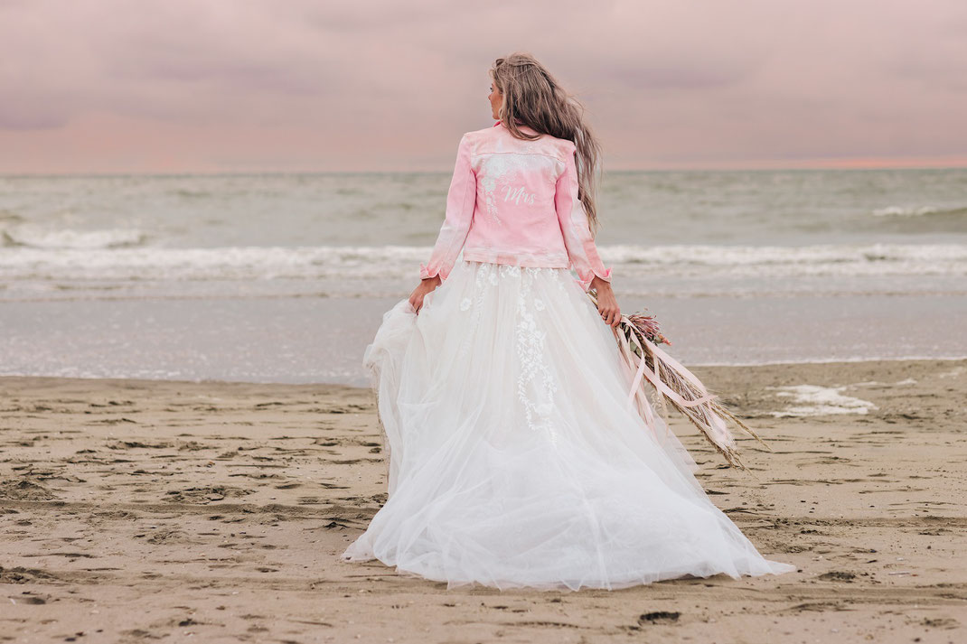 bruid draagt roze jasje beschilderd met witte bloemen, strandshoot bruiloft op strand