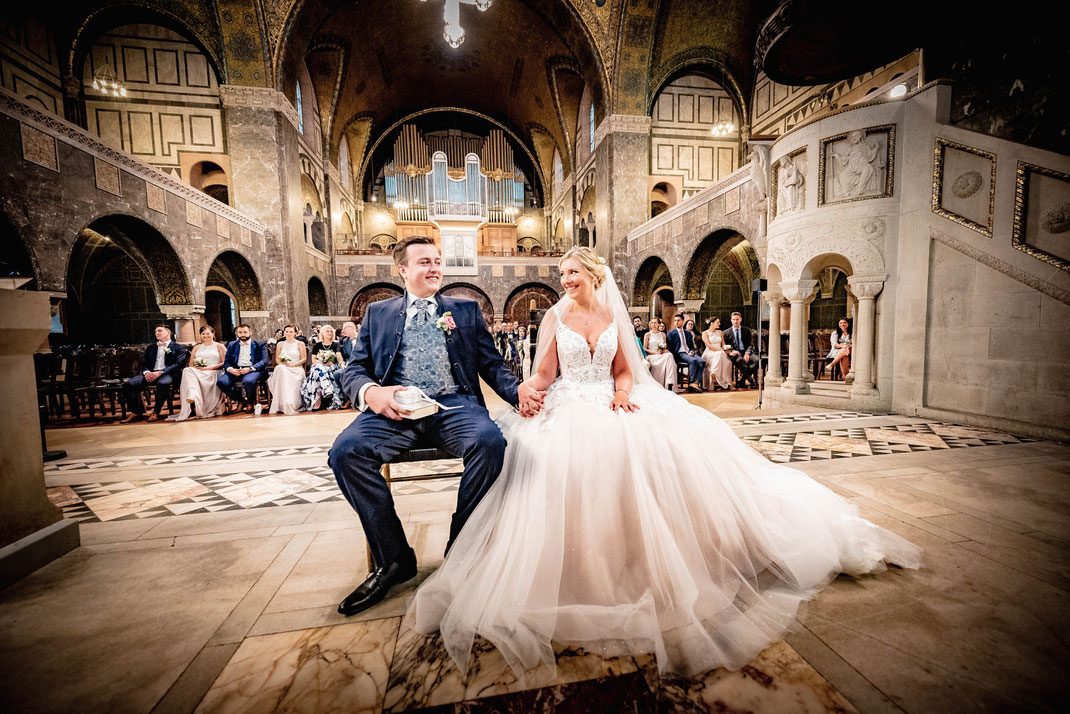 Ein Brautpaar sitz während ihrer Hochzeit in der Kirche und lächelt sich an.