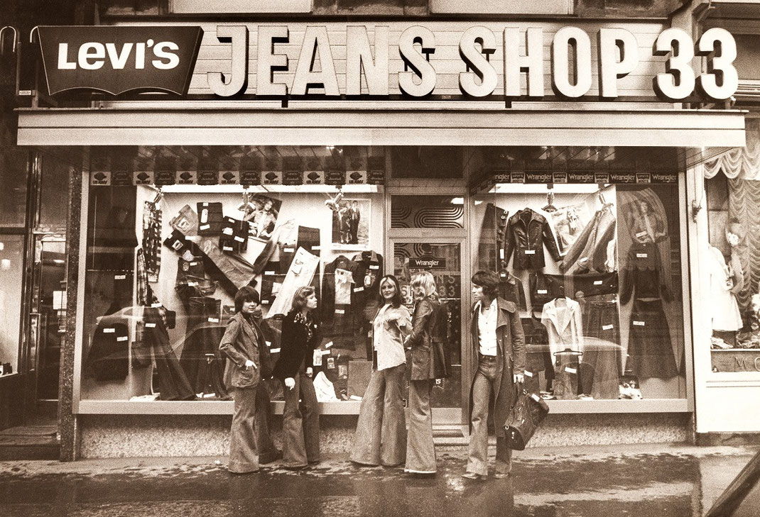 Schwarzweiss-Aufnahme von 1972, Jeans-Shop 33 Geschäftsportal davor der Gründer Marc Liberman und 4 Mitarbeiterinnen in damaliger Mode gekleidet