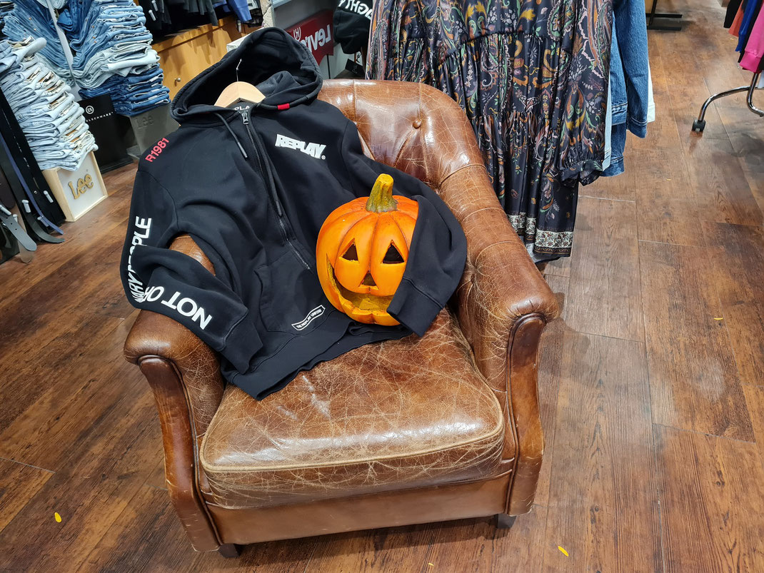Ein schwarzer Hoodie mit einem Deko-Kürbis auf einem Ledersessel in unserem Shop
