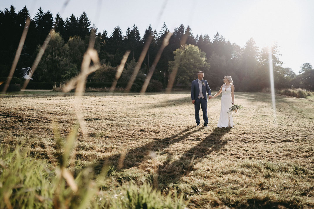Hochzeitsfotos zur Golden Hour im Erzgebirge. Das Licht streift von hinten die Kleidung. Auf der Wiese neben dem Waldhof Börnichen Erzgebirge