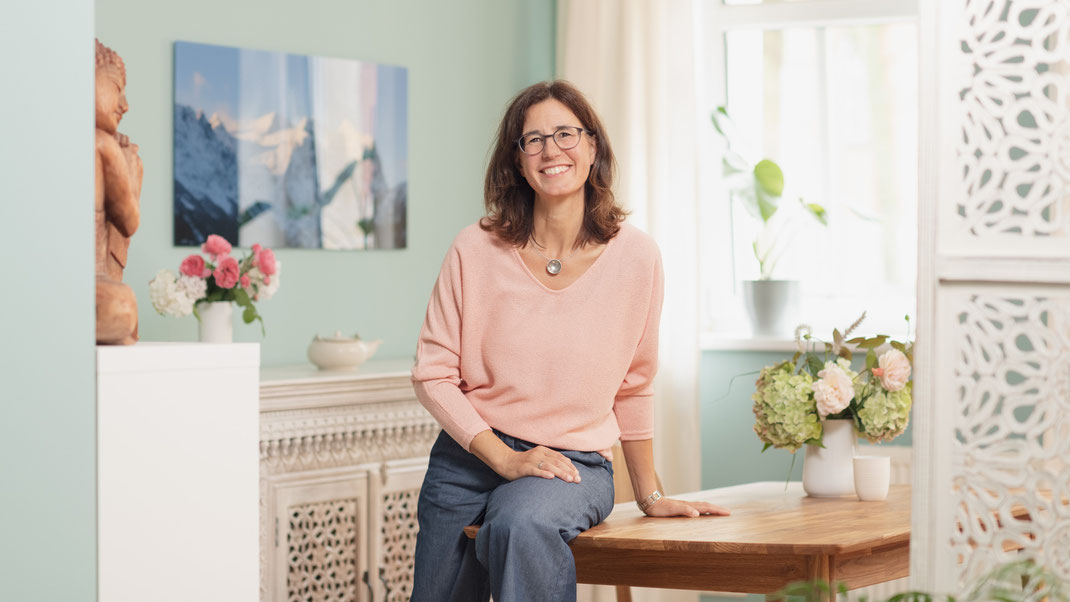 Stephanie Leßmann, Heilpraktikerin und Ayurveda Therapeutin sitzt am Tisch in ihrer Naturheilpraxis für Ayurveda und Ernährungsberatung in Weimar