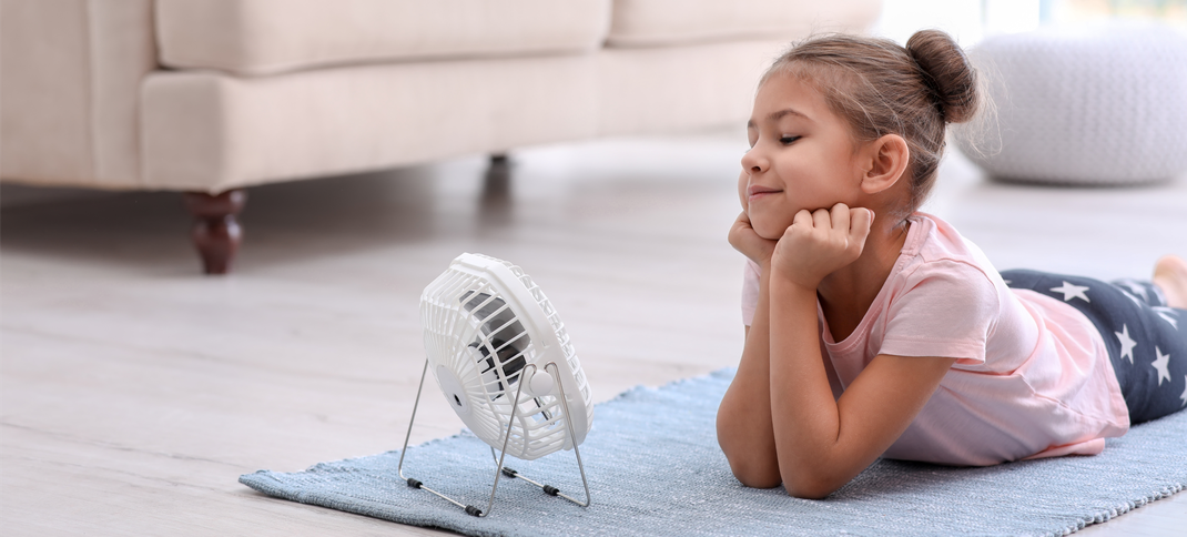 Mädchen liegt vor Ventilator auf dem Fußboden - Lüftung und Energiesparen