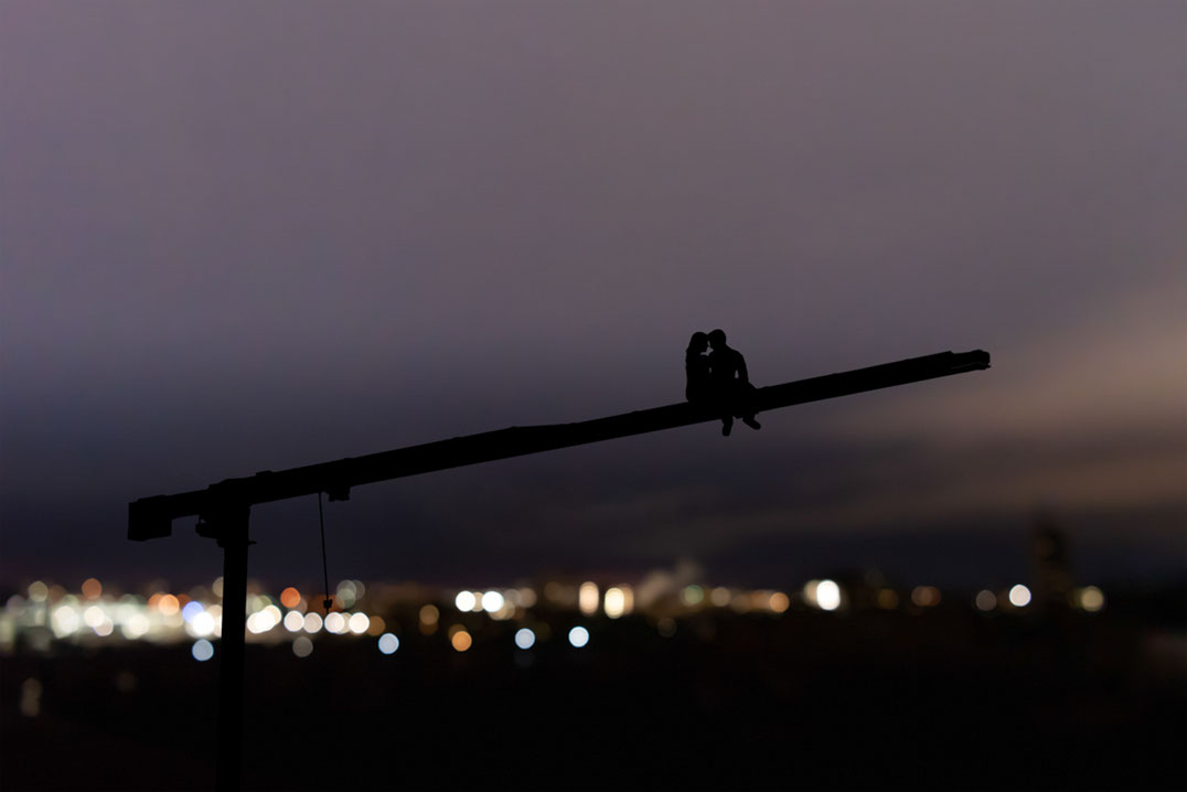 Male and female couple sitting on crane over city view at night. Couple is in silhouette. 