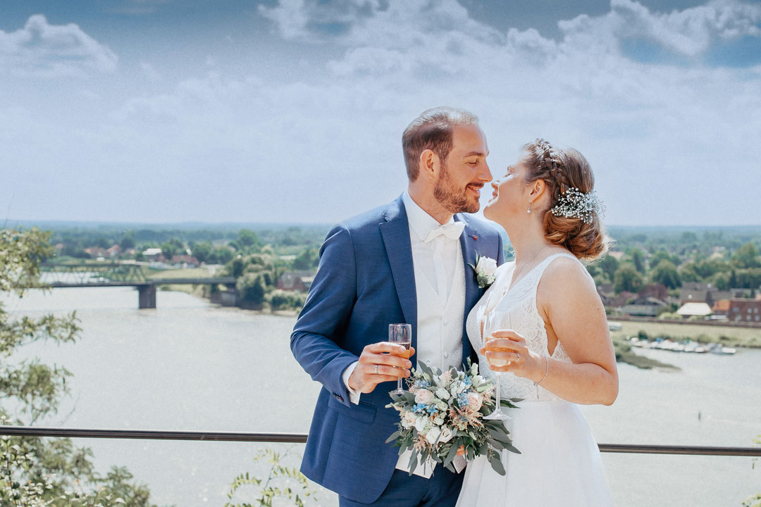 Brautpaar mit einem Glas Sekt zum Anstoßen nach der Trauung im Standesamt Lauenburg vor der Kulisse der Elbe