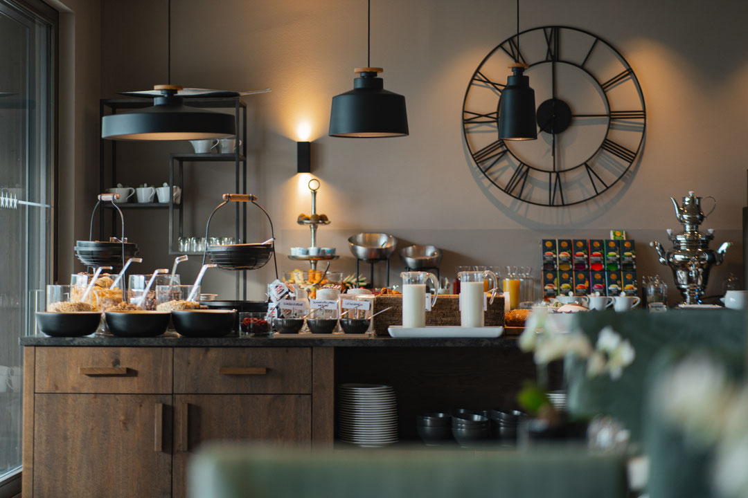 Modernes Frühstücksbuffet mit regionalen Spezialitäten, frischem Obst, Säften sowie Kaffee- und Teeangebot im stilvollen Speiseraum des Hotel Mair am Ort Living in Partschins bei Meran in Südtirol. Die warme Beleuchtung und das elegante Ambiente schaffen 