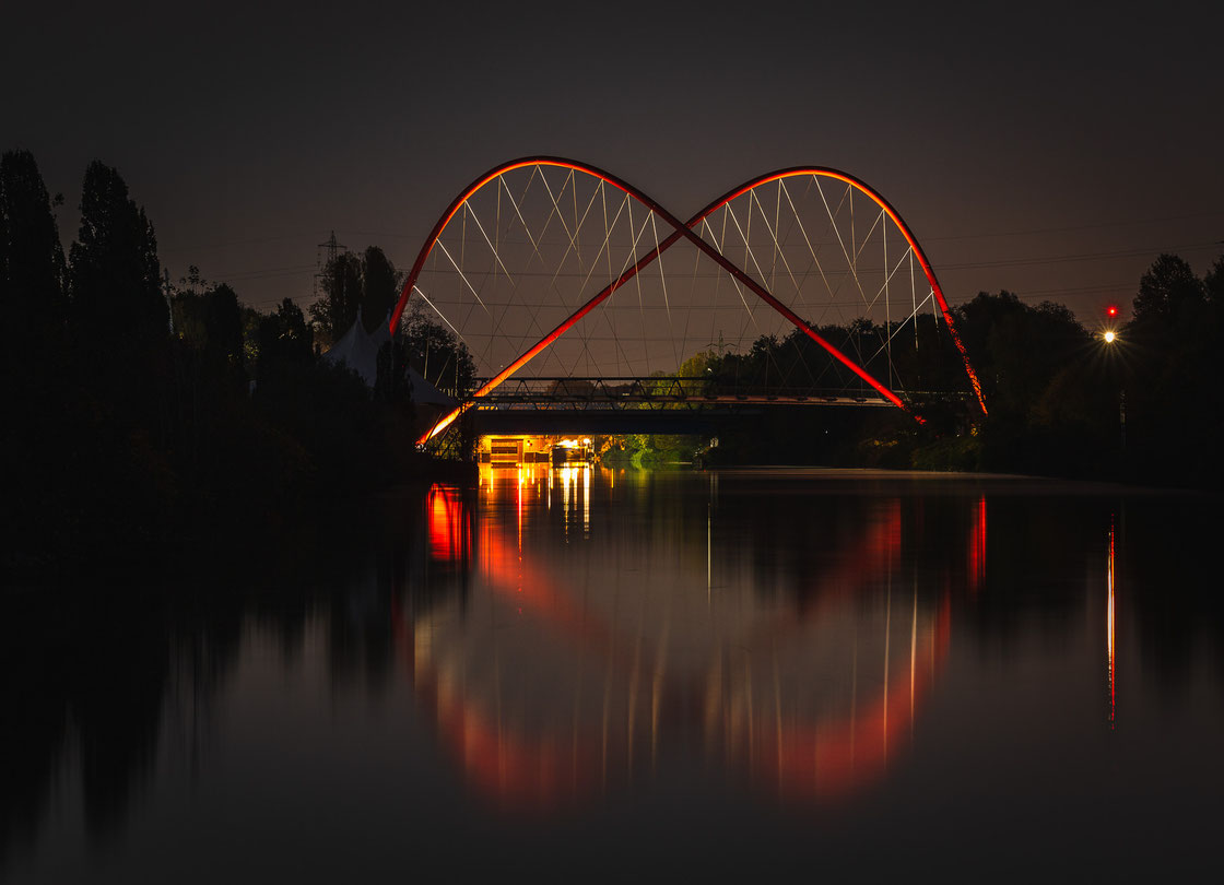Die beleuchtete Doppelbogenbrücke Nordsternpark in Gelsenkirchen bei Nacht mit Spiegelung im Rhein-Herne Kanal 