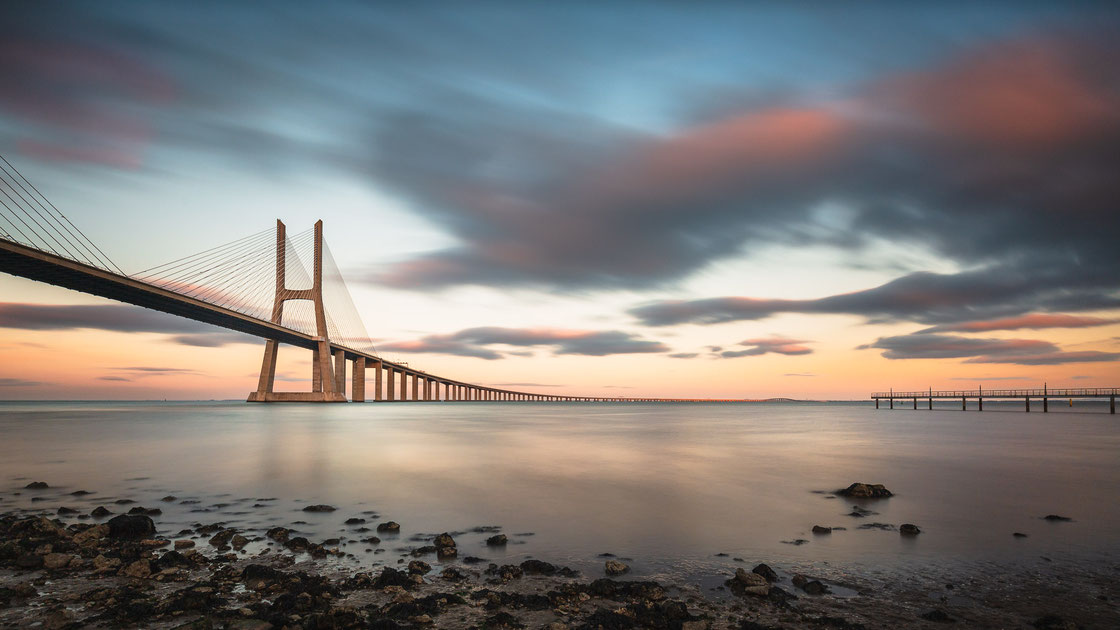 Langzeitbelichtung der Brücke Ponte Vasco da Gama an der Mündung des Flusses Tejo zwischen Lissabon und Setúbal in Portugal bei Sonnenuntergang (Architekturfotograf)