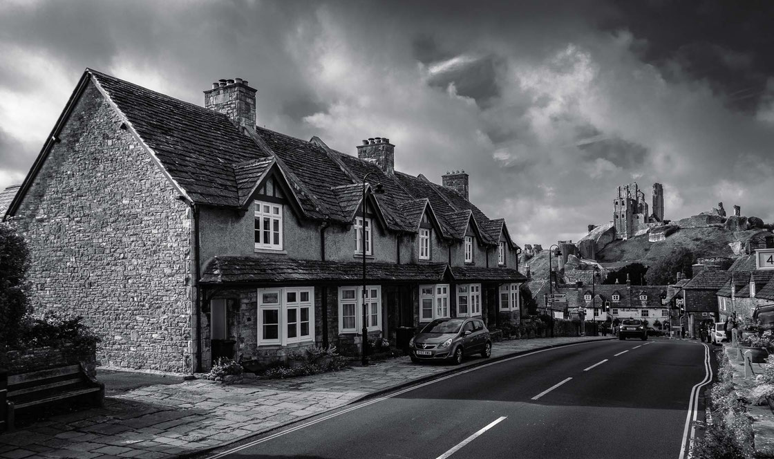 Schwarz-weiß Foto einer Häuserreihe mit Burgruine in Corfe Castle in Dorset in England