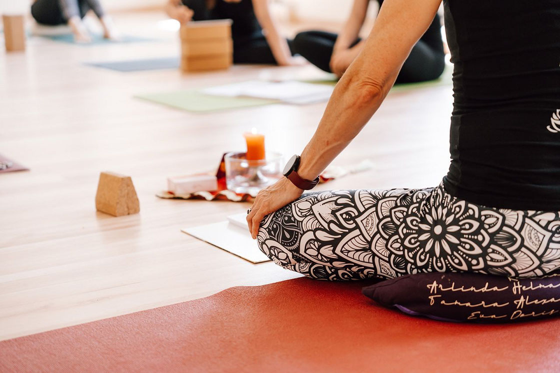 Teilnehmer einer Yogalehrer-Ausbildung in Oberösterreich sitzen im hellen Studio in Meditationshaltung.