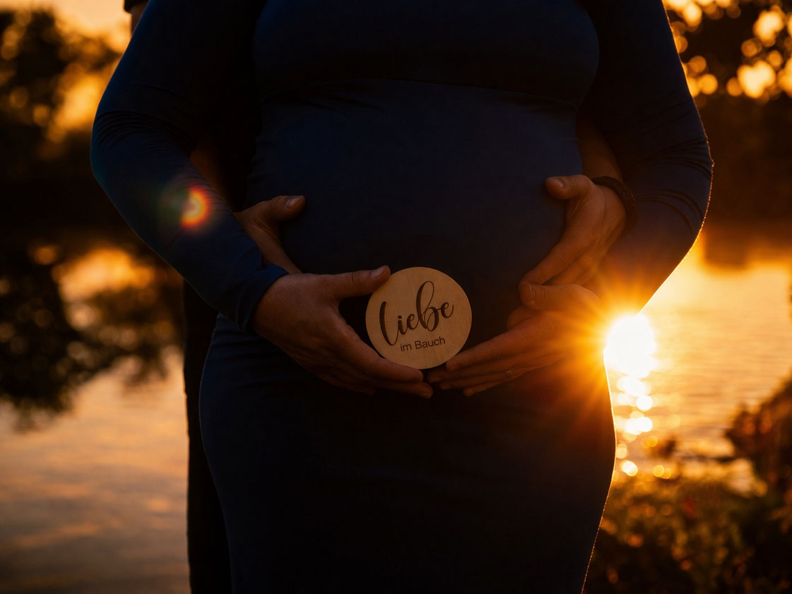 Detailaufnahme eines Babybauchs beim Babybauchshooting im Sonnenuntergang am See im Werra-Meißner-Kreis – Holzschild „Liebe im Bauch“