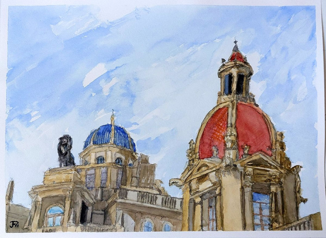 Dos cúpulas ornamentadas, una azul y otra rojiza, con una estatua de león sobre una cornisa y cielo claro de fondo.
