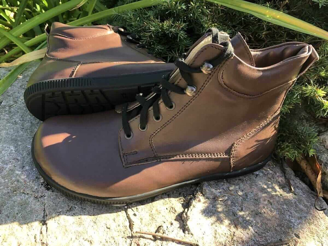 Barfuß Wanderstiefel aus braunem Leder liegen in der Natur auf einem felsigen Stein 