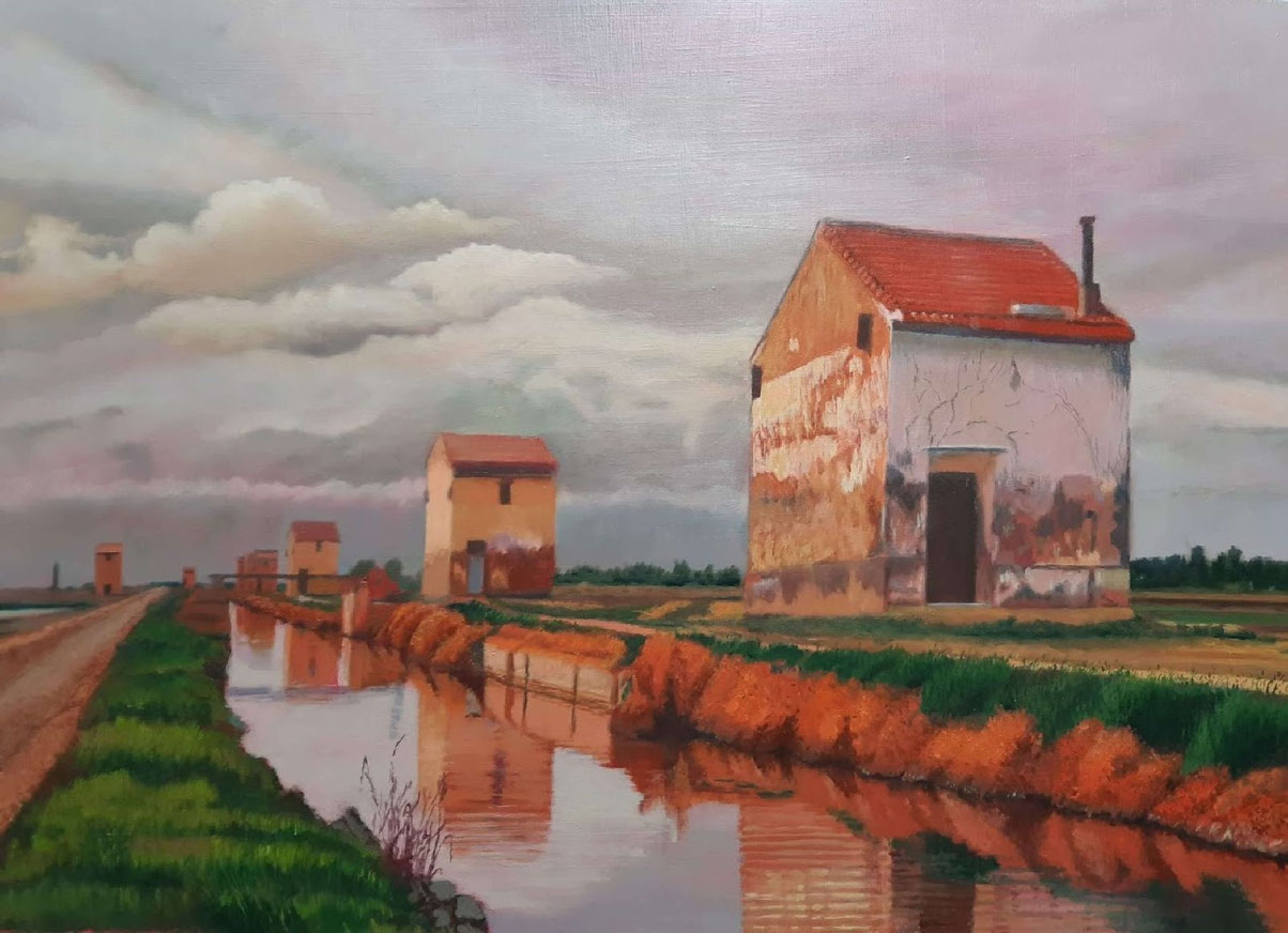 Casas rurales junto a un canal al atardecer, con reflejos en el agua y cielo parcialmente cubierto.