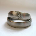Platin-Eheringe, Damenring mit funkelnder Diamantwelle, Herrenring schlicht mattiert.