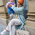 Mama sitzend hebt Baby hoch.