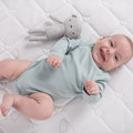 Fröhliches Baby mit Kuscheltier auf Babymatratze