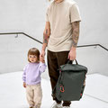 Papa mit Kind an der Hand und Wickelrucksack an der anderen Hand