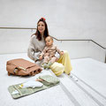 Mami mit Wickelutensilien und Baby sitzend auf einer Treppe.
