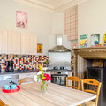 Espace repas lumineux avec cuisine fonctionnelle et ancienne cheminée dans la maison de vacances.