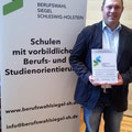 Schulleiter Lutz Glaeßner hält stolz die Plakette in der Hand