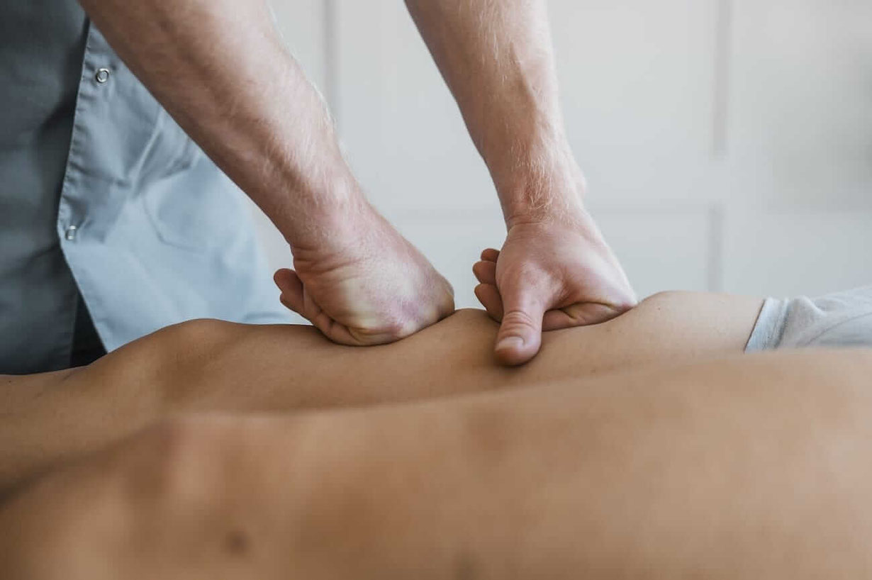 Faszientherapeut arbeitet mit beiden Fäusten an den Faszien des Oberschenkels einer liegenden Person
