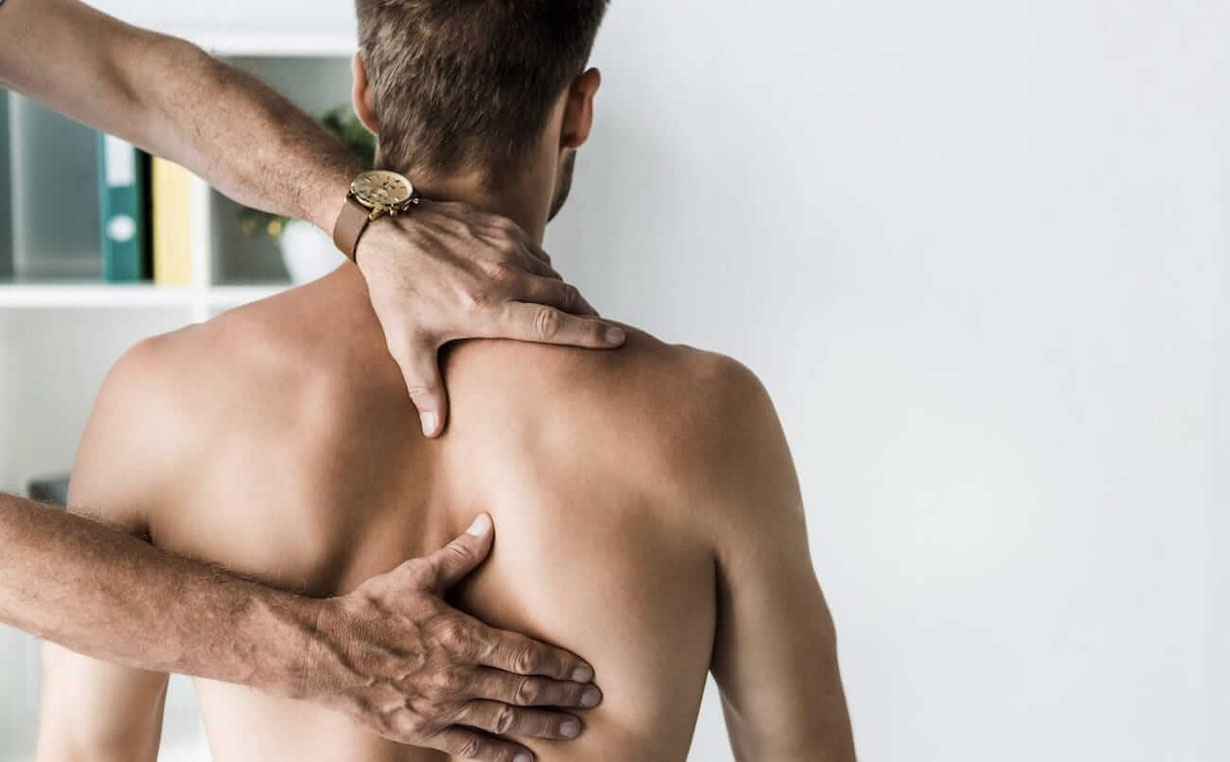 Mit Faszien Techniken wird das Schulterblatt eines aufrecht sitzenden Patienten behandelt