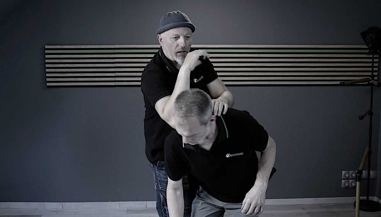Frank Demann schlägt mit dem Ellbogen in den Nacken einer Person die vornüber gebeugt vor ihm steht