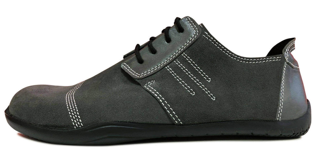 Flacher Barfußschuh komplett aus grauem Veloursleder mit weißen Nähten einer schwarzen Laufsohle und schwarzen Senkeln 