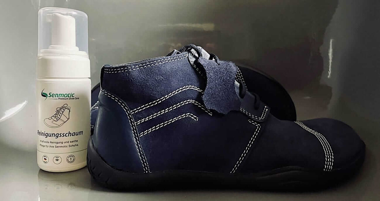 Eine Flasche Leder Reinigungsschaum von Senmotic steht neben einem dunkelblauen Barfußschuh mit weißen Nähten von Senmotic