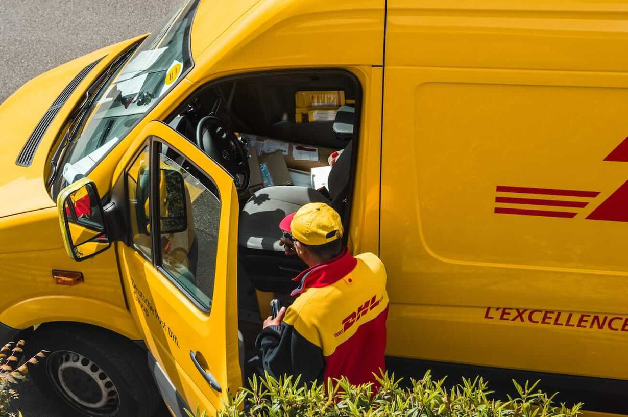Gelbes DHL Auto mit Fahrer in DHL Bekleidung und Basecape von DHL