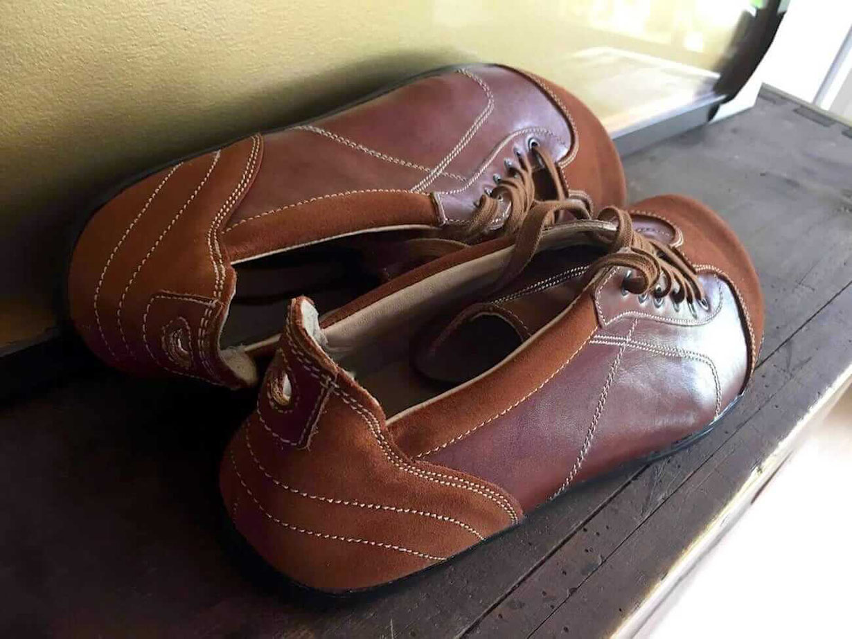 Senmotic Barfußschuhe aus braunem Leder liegen auf einem braunen Sideboard
