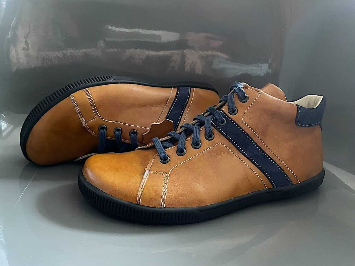 Barfußschuhe Modell 2Colours als halbhoher Stiefel aus braunem Leder mit Zierstreifen aus blauem Leder und blauen Applikationen aus Leder an der Ferse. Die Senkel sind Blau und die Sohle ist Schwarz