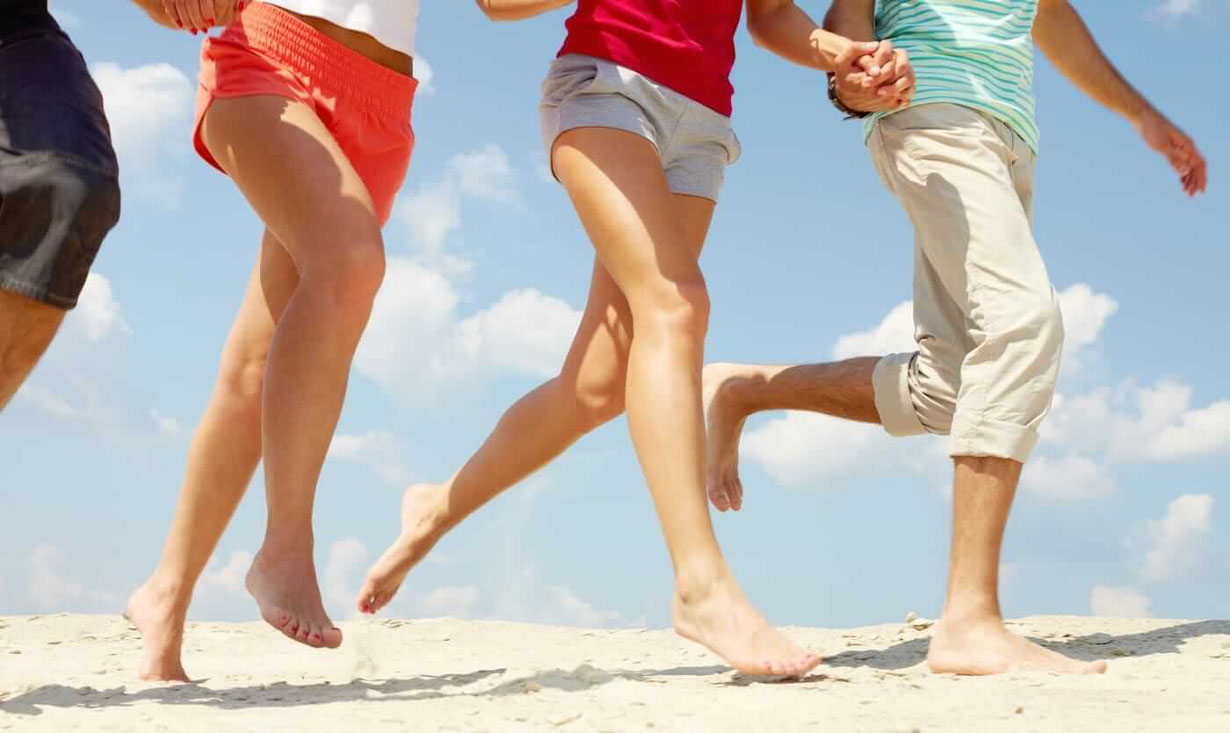 Drei Menschen laufen mit nackten Beinen und nackten Füßen im Ballengang über den Strand