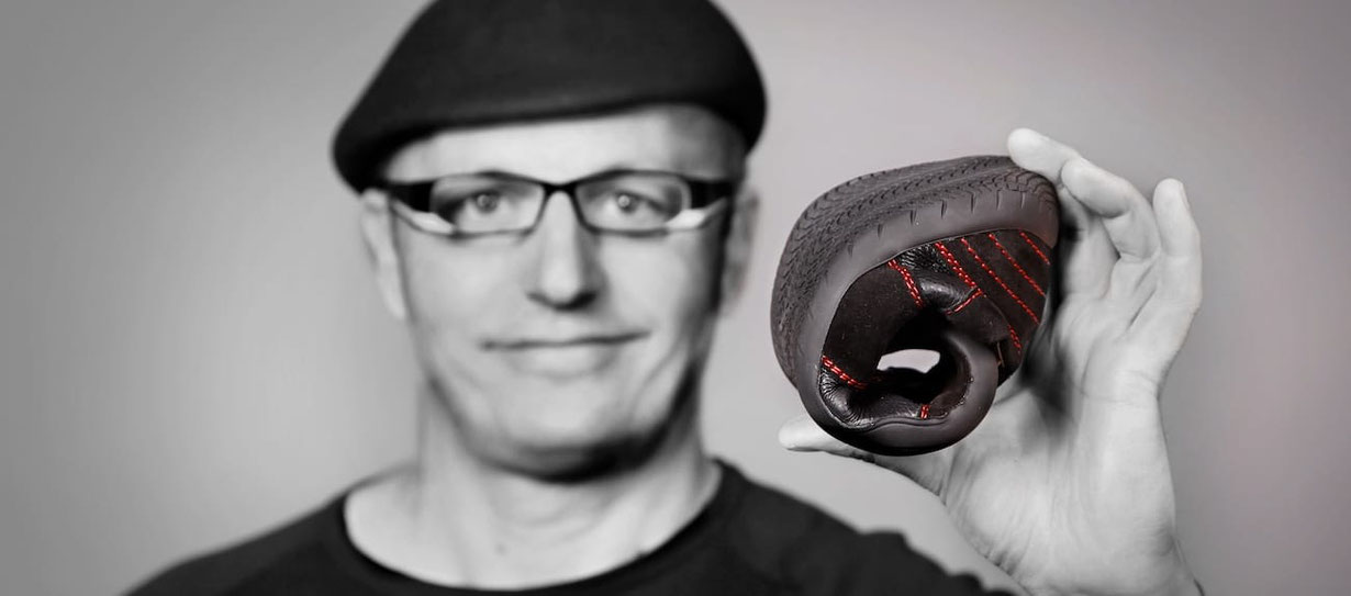 Ein Mann hält in einer Hand einen zusammengerollten Barfußschuh der Marke Senmotic