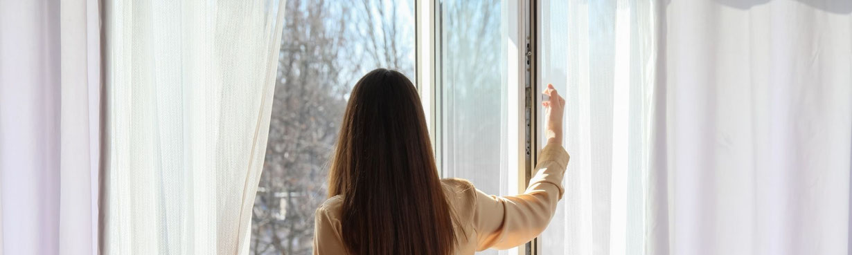 Frau in hellem Raum öffnet ein Fenster, Licht strömt hinein – Symbol für einen bevorstehenden inneren Wandel und den Beginn eines neuen Lebenskapitels.