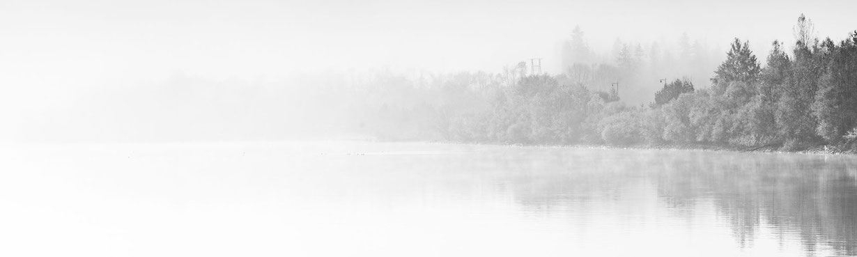 Ruhiger, nebliger See mit weiter Wasserfläche und Baumlinie als Symbol für Raum, Rückzug und Beziehung in Übergängen.