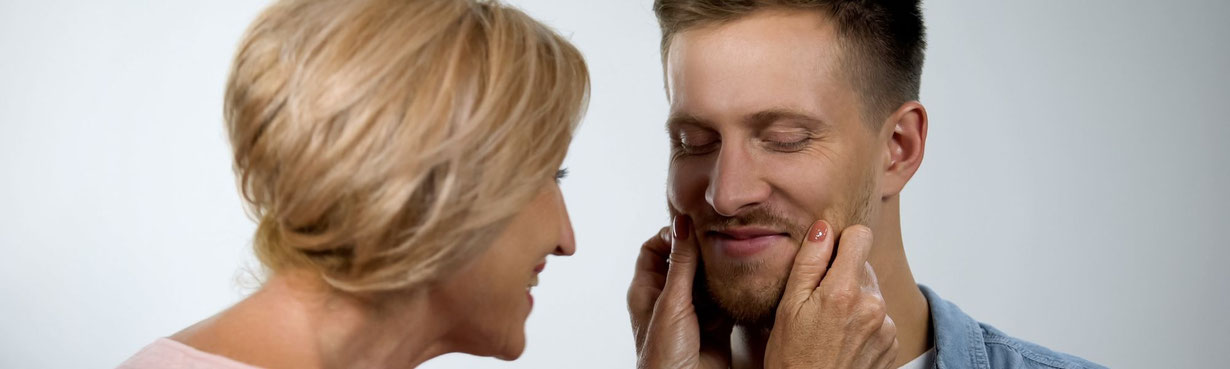 Mutter berührt das Gesicht ihres erwachsenen Sohnes liebevoll, Nähe und emotionale Bindung sind spürbar.