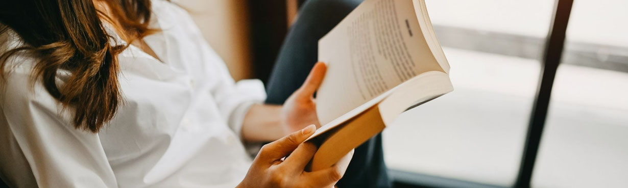 Frau sitzt am Fenster und liest ein Buch – ruhiger Moment der Inspiration und inneren Einkehr, passend zu spirituellen Buchempfehlungen.